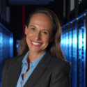 woman in power suit walking between rows of web servers in a data center toward the camera, zoomed in on her smiling face